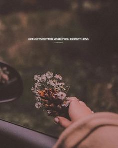 someone holding a flower in their hand with the words life gets better when you expect less