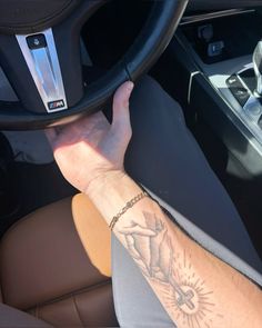 a person with a tattoo on their arm holding a steering wheel in a car,