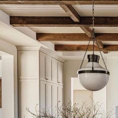 a chandelier hanging from the ceiling in a kitchen with white cabinets and wood beams