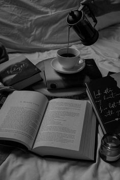 an open book sitting on top of a bed next to two coffee cups and books