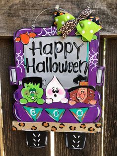 a sign that says happy halloween hanging on the side of a wooden fence with decorations