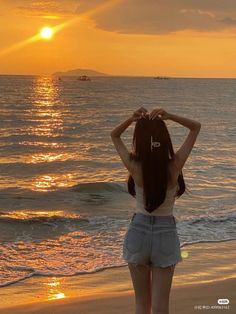 a woman standing on top of a sandy beach next to the ocean at sunset or sunrise