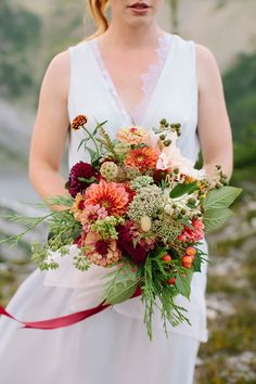 a woman in white dress holding a bouquet of flowers with red ribbon around her waist