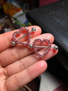 someone is holding two heart shaped pins in their hand and they are both wearing pink crystals