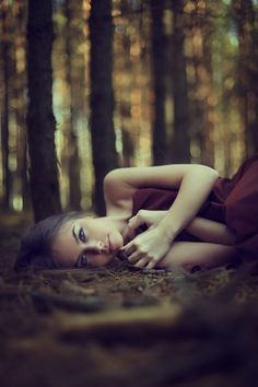 a woman laying down in the woods with her hands on her chest and eyes closed