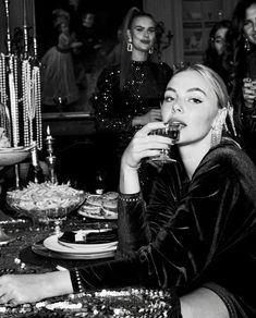 a black and white photo of a woman sitting at a table with other women in the background