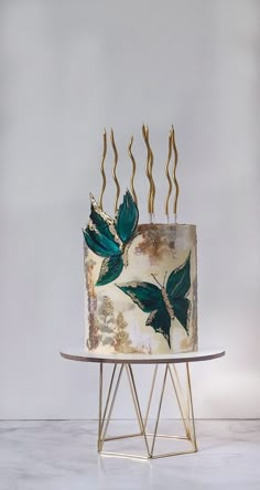 a white cake with green leaves on it sitting on top of a metal stand in front of a gray wall