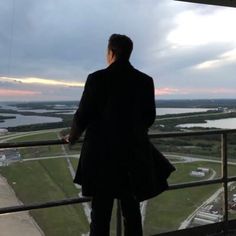 a man standing on top of a tall building looking out over a field and river