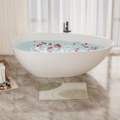 a white bath tub sitting on top of a bathroom floor next to a rug and towel