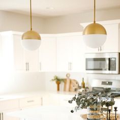 two lights hanging over a kitchen island in a white and gold colored kitchen with stainless steel appliances