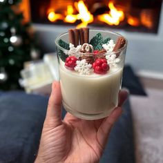 a person holding up a small glass with food in front of a fire place and christmas decorations