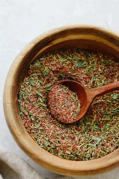 a wooden bowl filled with spices on top of a white table cloth next to a wooden spoon