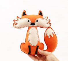 a hand holding an orange and white felt fox ornament in it's right hand