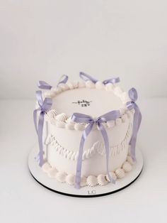 a white cake with purple ribbon and seashells on the top is sitting on a plate