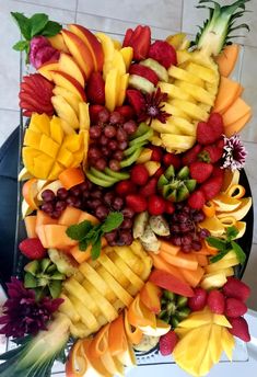 a bunch of fruit is arranged on top of a plate with grapes, strawberries, pineapples and other fruits