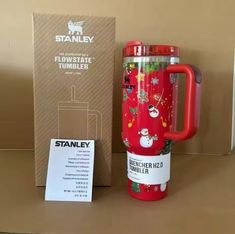 a red travel mug sitting on top of a table next to a box and card