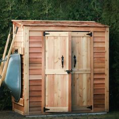 a wooden shed with two doors and an open door on the side, in front of some trees