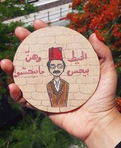 a hand holding up a wooden coaster with an image of a man wearing a red hat