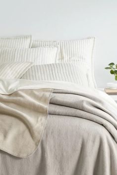 an unmade bed with white sheets and pillows on top of it, next to a potted plant