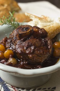 a white bowl filled with meat and beans on top of a table next to bread