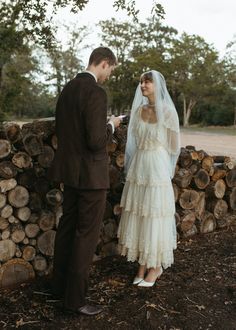 a bride and groom standing next to each other in front of a pile of logs