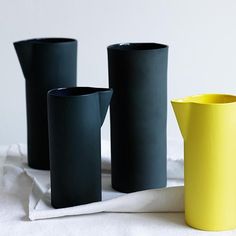 three black and yellow vases sitting on top of a white table cloth next to each other