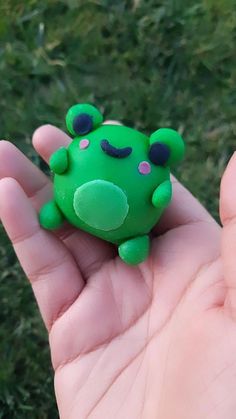 a small green frog toy sitting on top of someone's hand in the grass