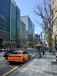 an orange car is parked on the side of the road in front of tall buildings