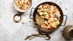 a pan filled with pasta and sauce next to two spoons on top of a table