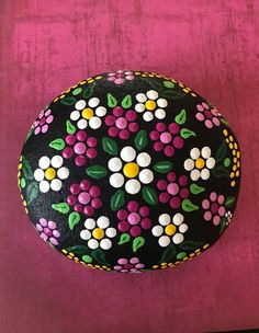 a painted rock sitting on top of a pink table next to a purple wall with white and yellow flowers