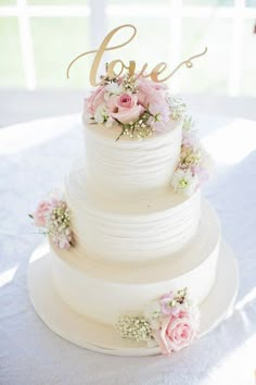 a white wedding cake with pink flowers and the word love on top is sitting on a table