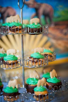 cupcakes with green frosting and animals on them are arranged in tiered trays