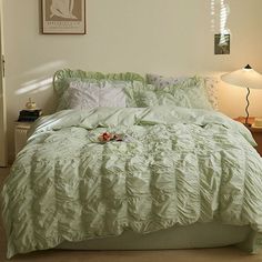 a bed with green comforter and pillows in a room next to a lamp on a table