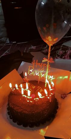 a birthday cake with lit candles on it sitting in front of a balloon that says happy birthday