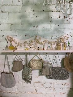 several purses are hanging on a white brick wall next to a shelf with other purses