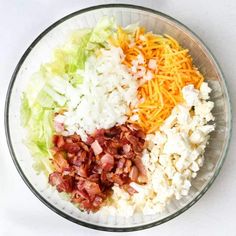 a bowl filled with lettuce, cheese and bacon on top of each other