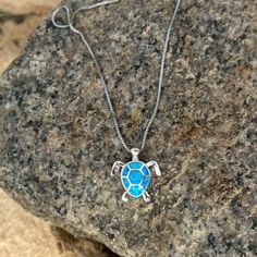 a necklace with a blue turtle on it sitting on top of a large stone slab