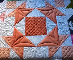 an orange and white quilt on top of a bed with many different colored squares in it