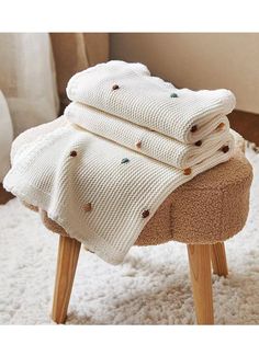 three blankets stacked on top of each other on a stool in a room with white carpet