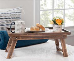 a tray with bread and coffee on it in front of a window next to a couch