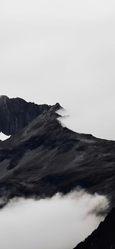 an airplane flying over the top of a mountain covered in fog and clouds on a cloudy day