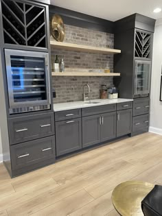 a kitchen with gray cabinets and white counter tops, wood floors and a brick wall