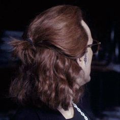 a woman with long hair wearing glasses and a chain around her neck is looking off into the distance