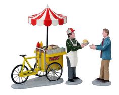 two figurines are standing next to each other near a cart with food on it