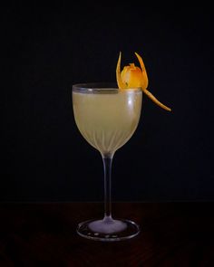 a glass filled with a drink sitting on top of a wooden table next to a black wall