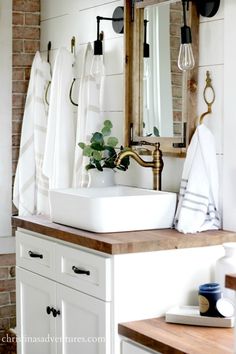 a bathroom sink sitting under a mirror next to a wooden counter top with towels hanging on it