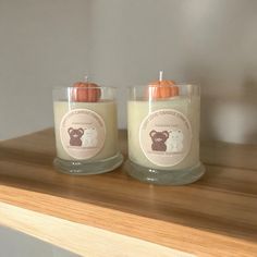 two candles sitting on top of a wooden shelf next to each other, one with an orange candle in it