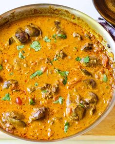 a pan filled with meat and vegetables covered in sauce on top of a wooden cutting board