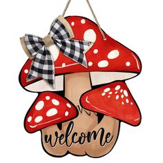 a wooden welcome sign with red mushrooms and gingham bows on it's head