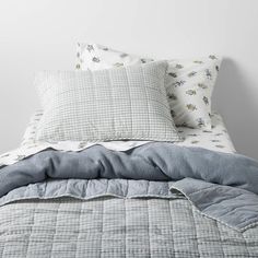 an unmade bed with grey and white sheets, pillows and blankets on top of it